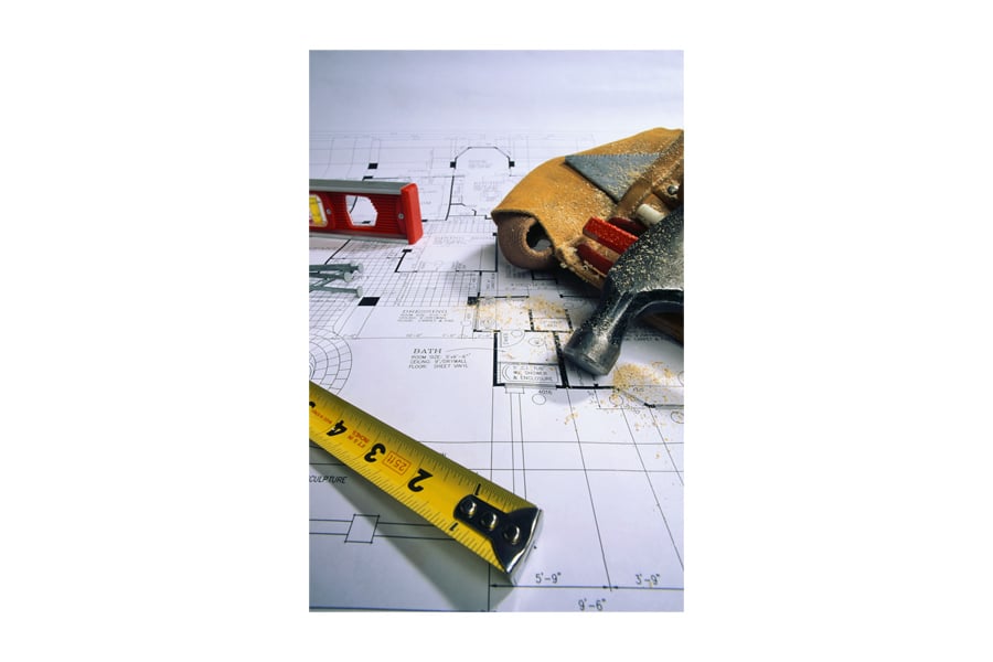 Picture of blueprints with a tape measure, level, nails and a tool belt laying on top